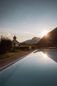 Swimming pool by lake against sky during sunset