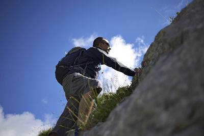 Low angle view of hiker climbing mountain against sky during sunny day
