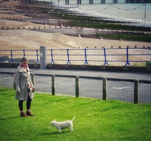 Full length of woman with dog standing on grass in park