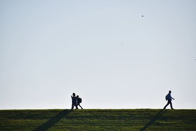 Low angle view of people walking on field against clear sky