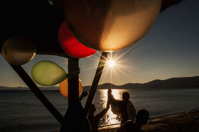 Silhouette people enjoying at beach against sky during sunset