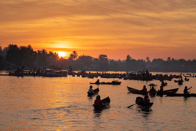 Silhouette people swimming in lake against sky during sunset