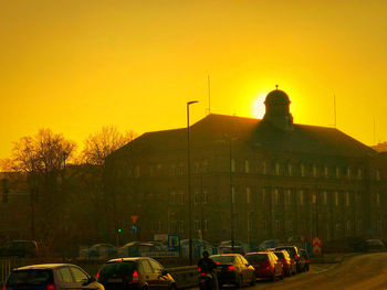 Cars on street by buildings against sky during sunset