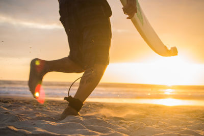 Man surfing on beach against sky during sunset