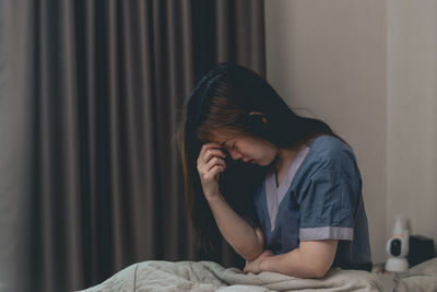 Side view of young woman sitting on bed at home
