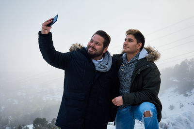 Two guys pose and take a picture with their phone surrounded by snow