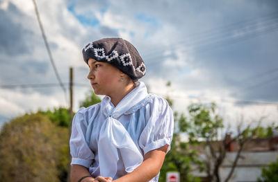 Low angle view of thoughtful teenage girl wearing cap while standing against sky