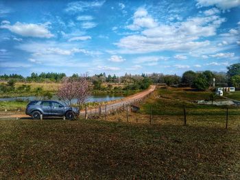 Cars on road by field against sky