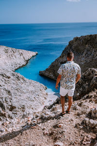 Rear view of man standing on rock while looking at sea