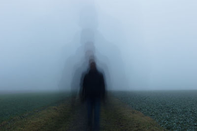 Rear view of people walking on field during foggy weather