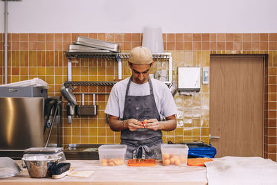 Male baker wearing apron standing at table in bakehouse and preparing fresh fruits for cooking