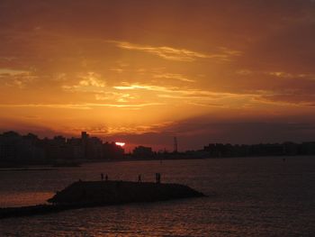 Silhouette buildings by sea against sky during sunset