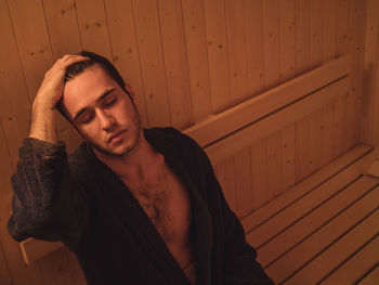 Young man wearing bathrobe relaxing in sauna