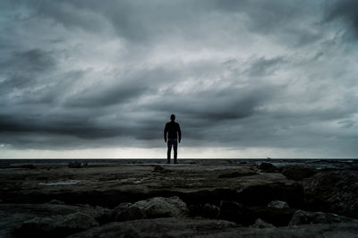 Rear view of silhouette man standing on rock against sky