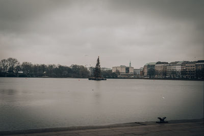 View of buildings by river against cloudy sky