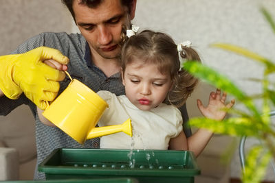 Father and daughter watering plant at home