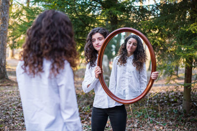 Woman reflecting in mirror held by friend while standing on field