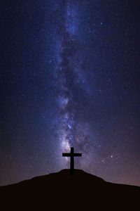 Silhouette cross on field against sky at night