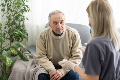 Caring nurse talks to old patient holds his hand sit in living room at homecare visit provide