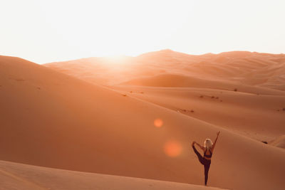 Yoga pose on desert at scenic view of sunset sky