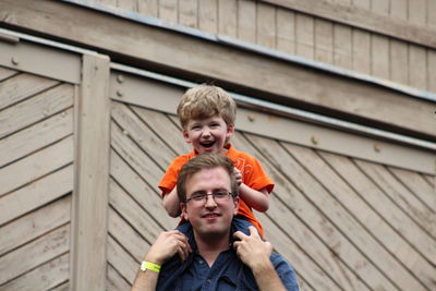 Portrait of smiling father carrying son on shoulder against wall