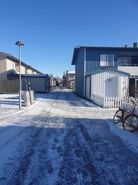 Snow covered street by buildings against clear blue sky