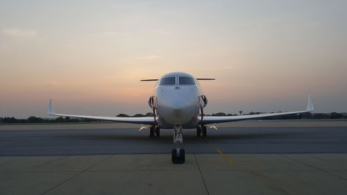 Airplane on runway against sky during sunset