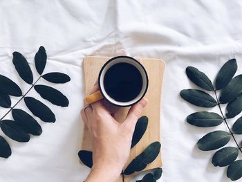 Directly above shot of woman holding coffee cup on table at home