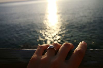 Close-up of hand against sea during sunset