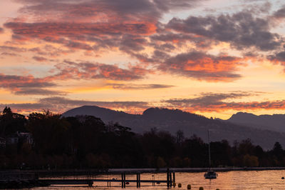 Scenic view of lake by silhouette mountains against orange sky