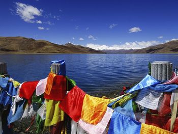 Colorful prayer flags hanging on fence at lakeshore against sky