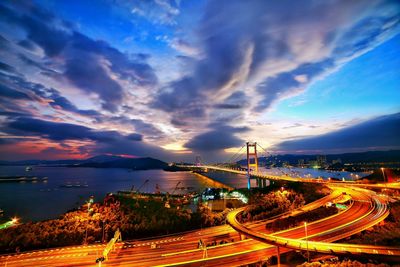 Aerial view of illuminated suspension bridge over river against cloudy sky