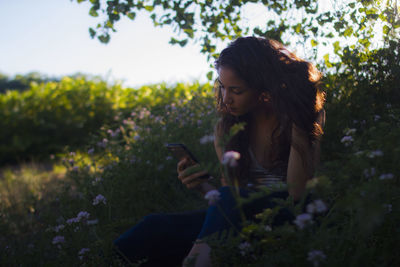 Young woman using phone while standing by plants