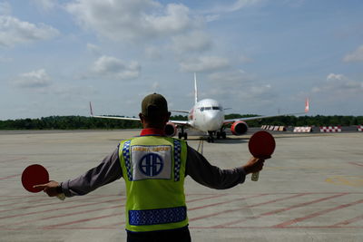 Rear view of man standing on airplane against sky