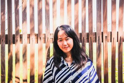 Portrait of beautiful young woman standing against fence