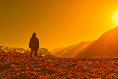 Rear view of man walking on mountain against sky during sunset