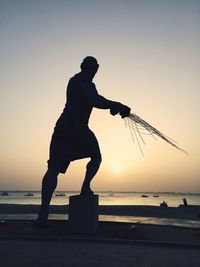 Silhouette statue at beach against clear sky during sunset