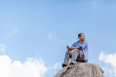 Low angle view of man sitting on rock against sky