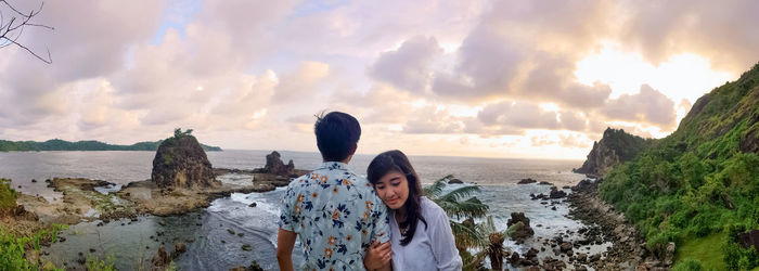 Young couple standing at beach against sky during sunset