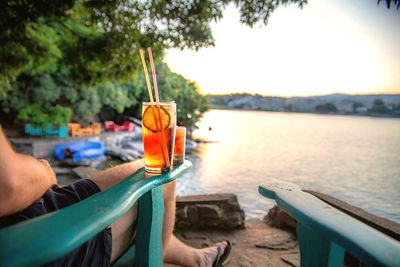 Cropped image of man with drink glass at beach during sunset