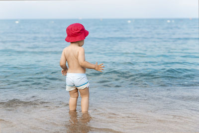 Rear view of shirtless boy standing on beach