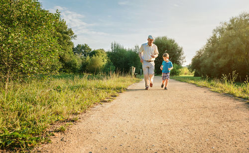 Grandfather and grandson running on footpath against sky