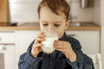 Little boy sitting in the kitchen and drinking milk. fresh milk in glass, dairy healthy drink. 