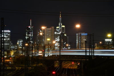 Illuminated street amidst buildings against sky at night