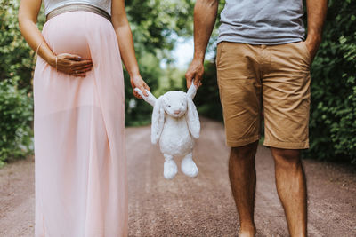 Midsection of pregnant woman with husband holding toy against trees