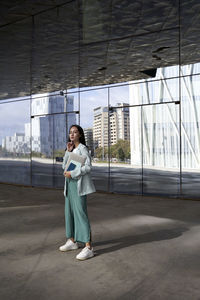 Full length portrait of a smiling young woman holding mobile phone