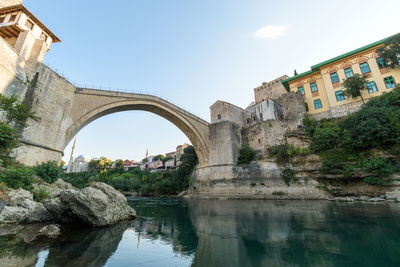 Arch bridge over river by buildings against sky