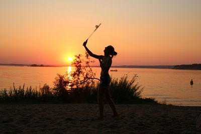 Woman playing tennis at beach against sky during sunset