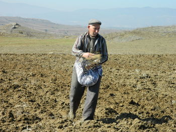 Man scattering seed while standing on field against sky