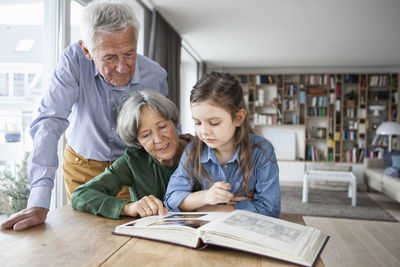 Grandparents watching photo album with their granddaughter at home